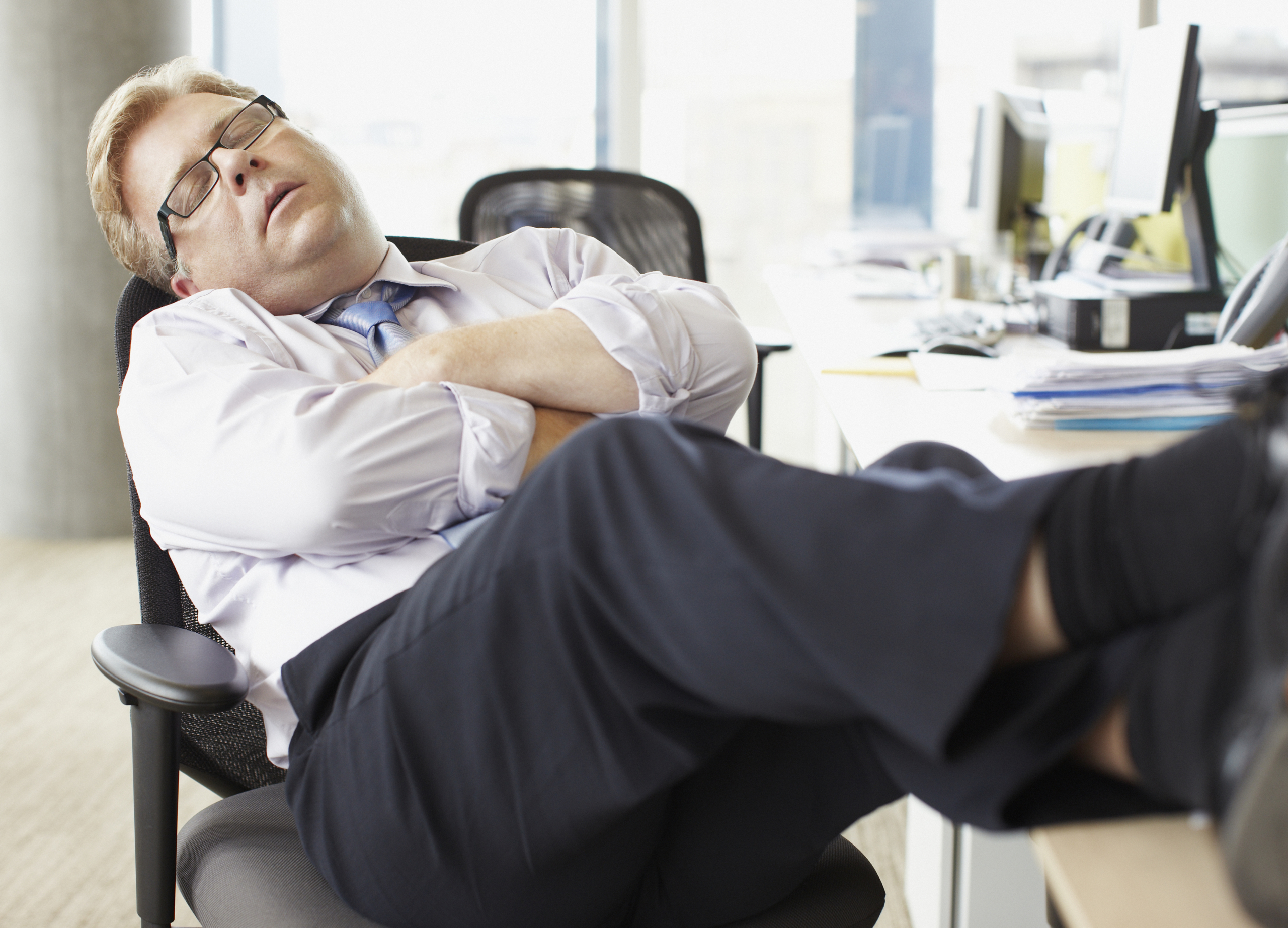 Businessman sleeping with feet up at desk Siesta im Büro