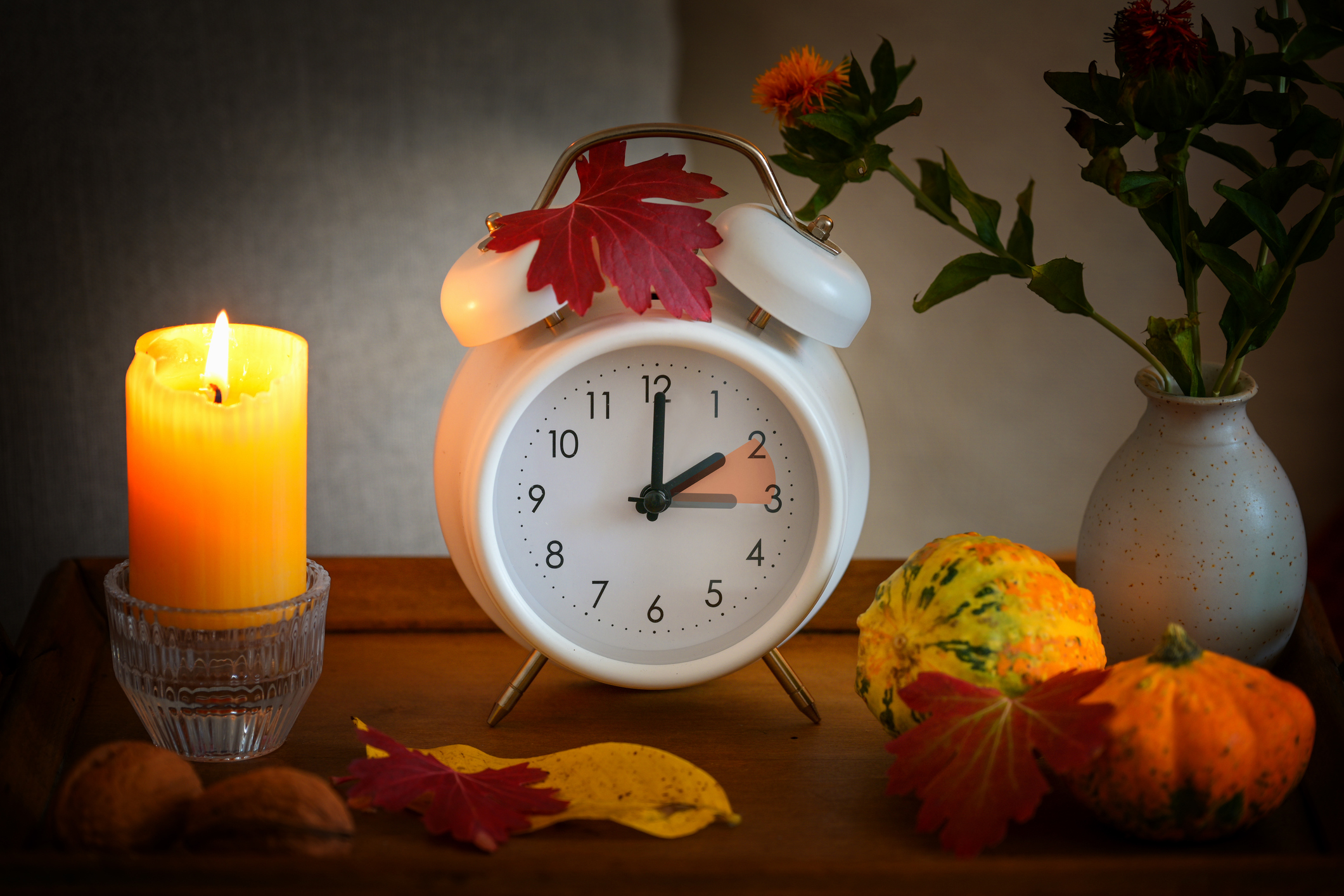 Fall back, time change on a white alarm clock after daylight saving time, candle, leaves and pumpkins as autumn decoration Uhr mit Zeitumstellung